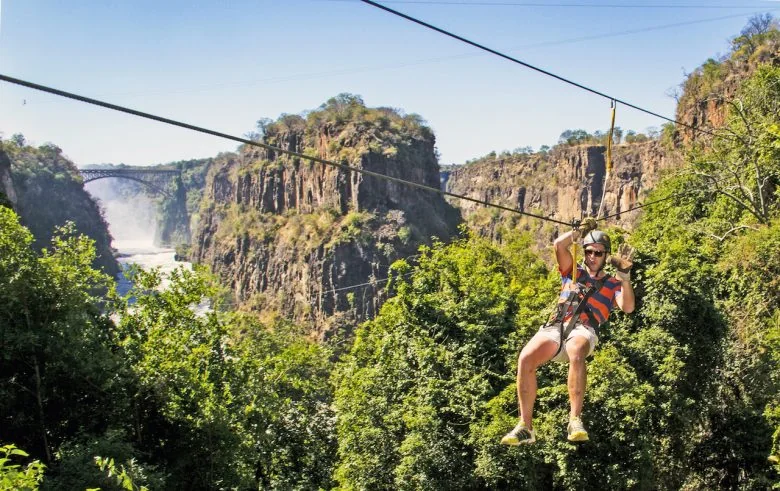 Harnessed visitor riding a canopy cable above the wooded gorge