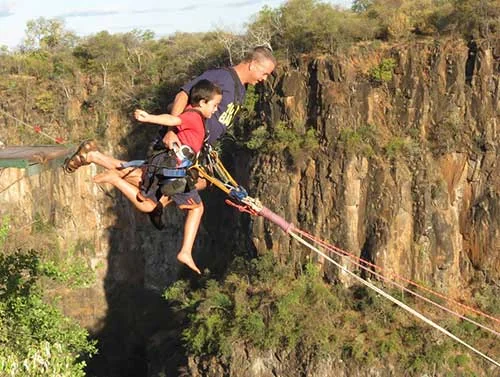 Two harnessed visitors launching together from a gorge swing platform