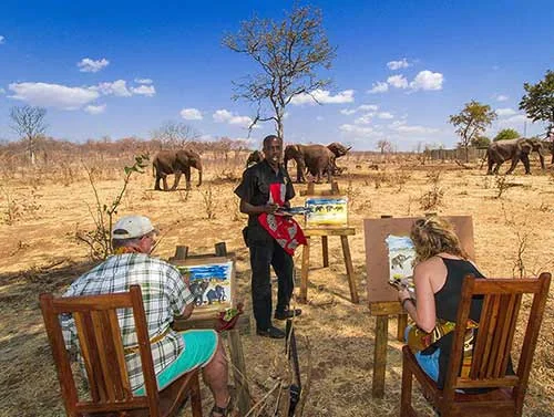 Visitors painting outdoors with elephants in the background