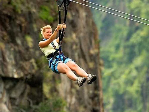 Harnessed visitor riding a zipline across a wooded gorge